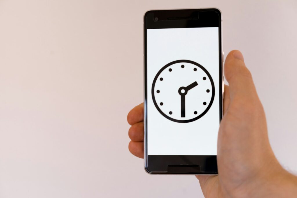 Hand holding a smartphone that shows a clock on its screen
